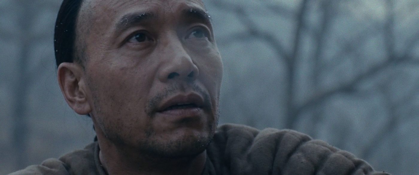 A man's face in cold grey light, looking upward.
